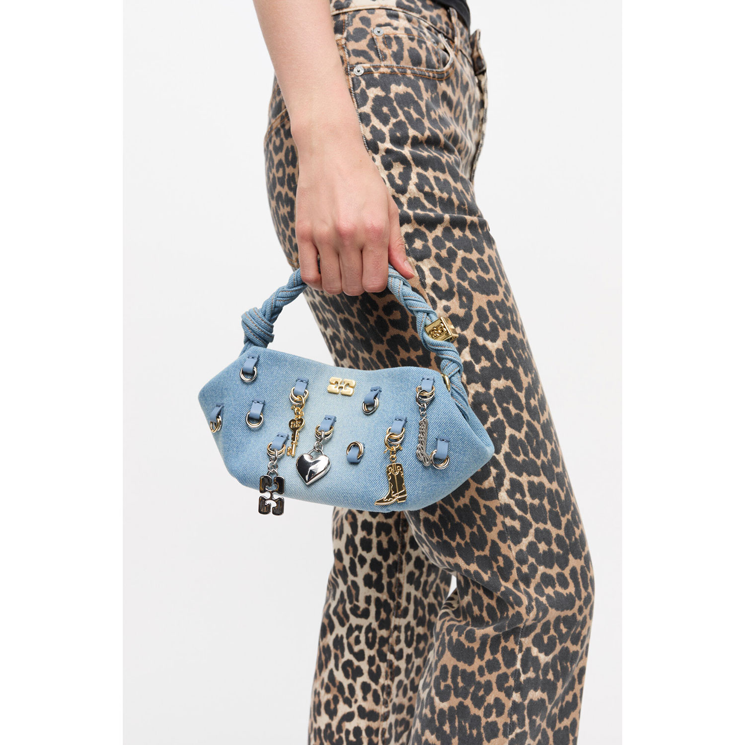 Ganni A6512 Bou Mini Tasche mit gold- und silberfarbenen Charms aus hellblauem Denimstoff von Ganni. Model seite