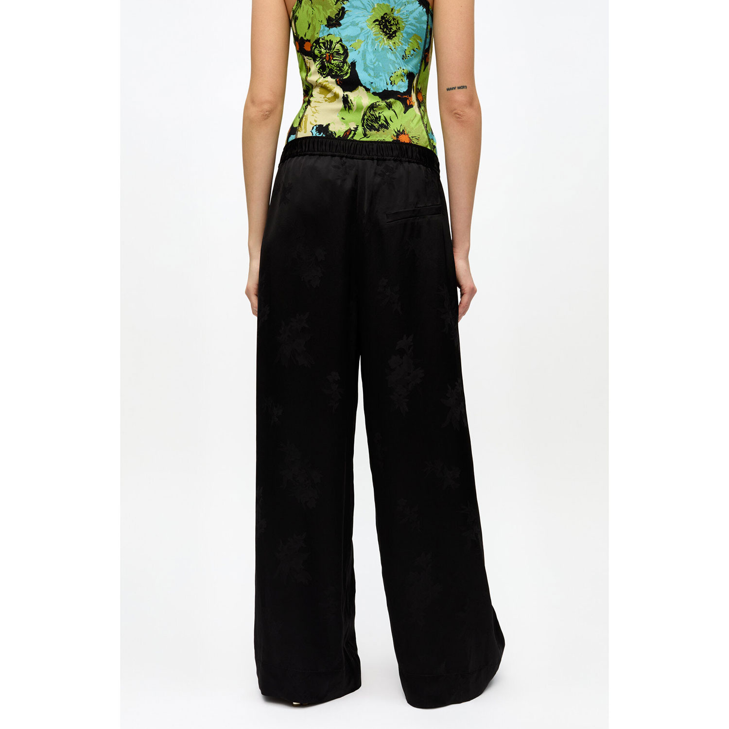 Ganni W0383 Satin Jacquard Hose in Schwarz mit zartem Blumenmuster, elastischem Bund und weiten Beinen von Ganni. Model hinten